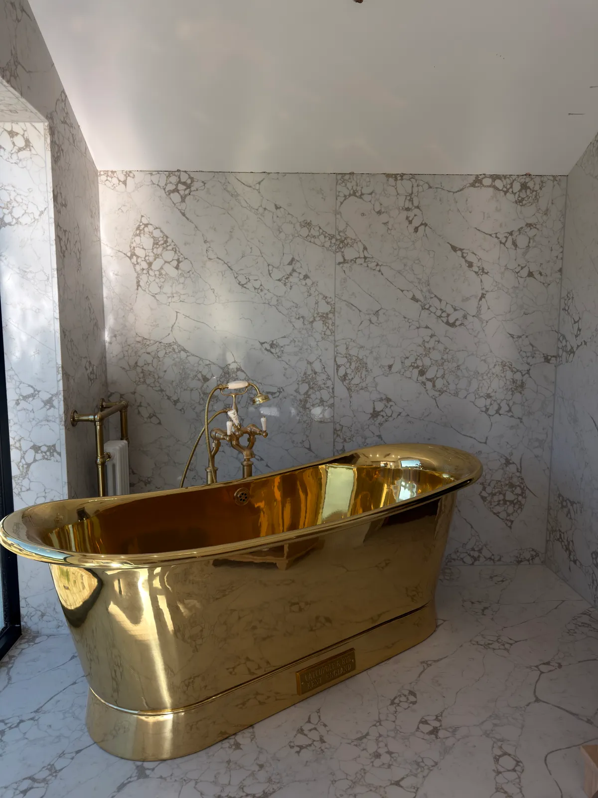 A gold coloured freestanding bath beside pale veined quartz slabs in the Knutsford bathroom.